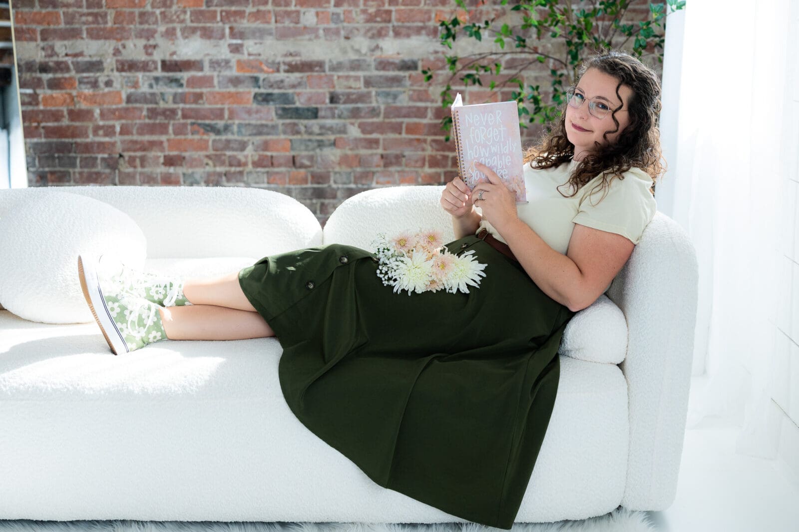 Emma Males sitting on a couch with a notebook looking at the camera. Emma is an SEO expert